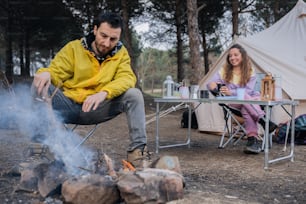 a man and a woman sitting at a table next to a campfire