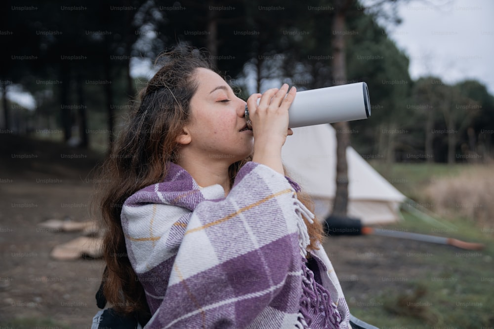 a woman with a blanket wrapped around her is drinking from a cup