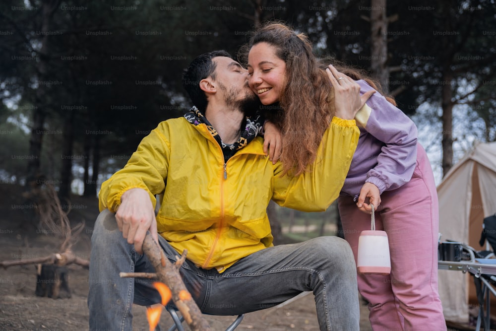 a man and woman sitting next to a campfire