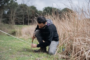 a man kneeling down in a field holding a stick