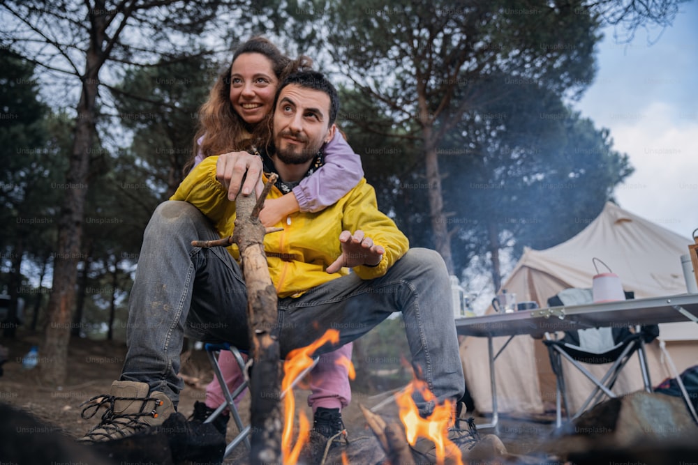 a man and woman sitting on a log in front of a campfire