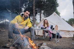 a man and a woman sitting at a table in front of a campfire