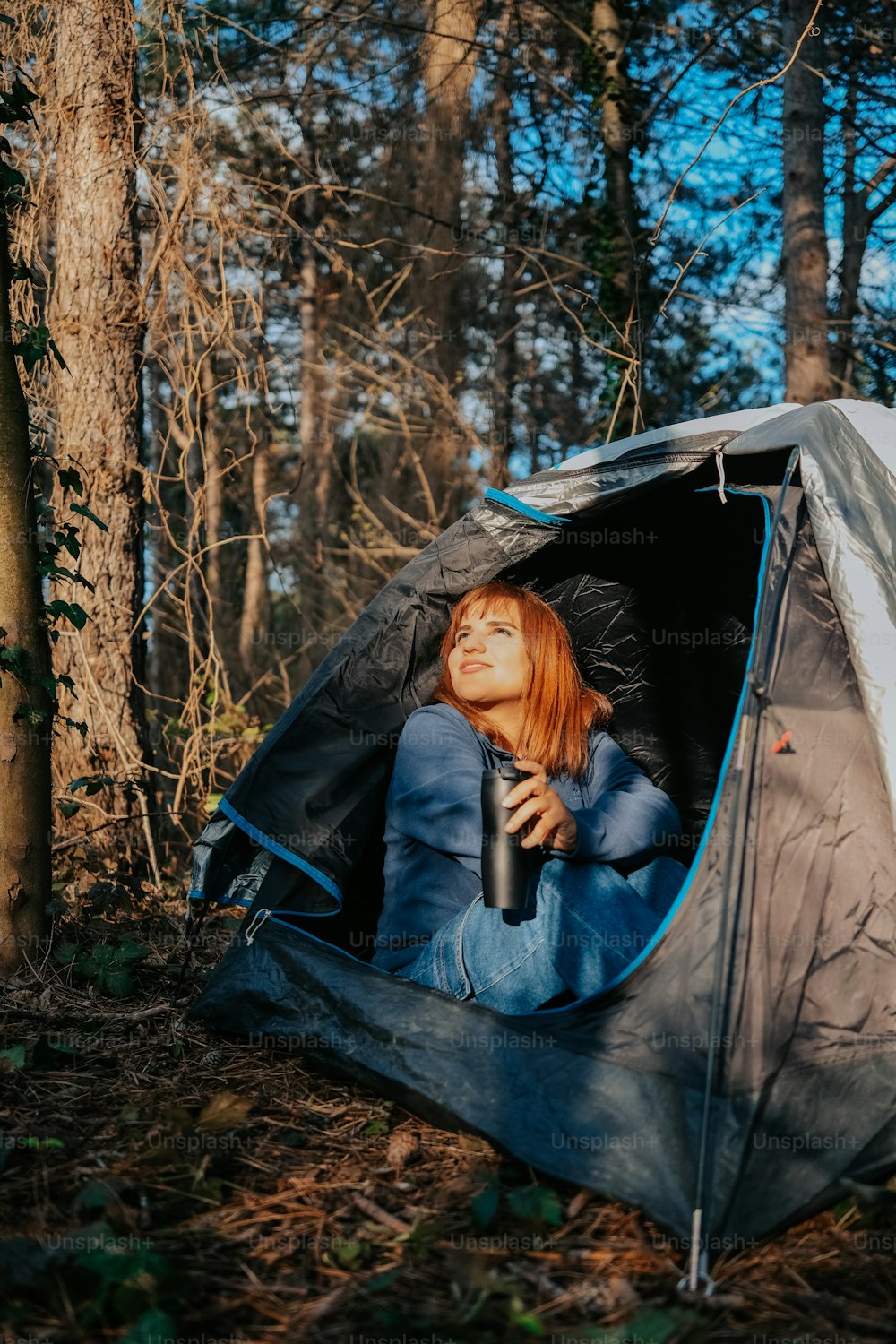 a woman sitting inside of a tent in the woods