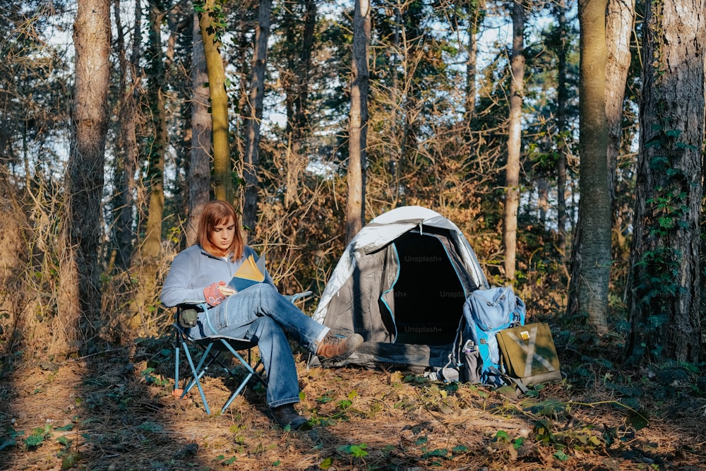 uma mulher sentada em uma cadeira ao lado de uma tenda na floresta