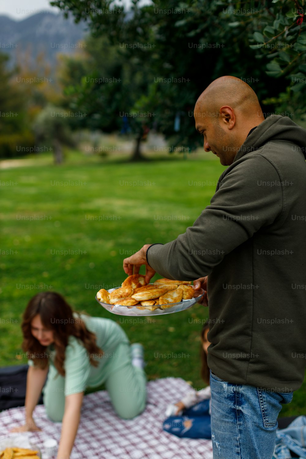 a man holding a plate of food on a picnic blanket