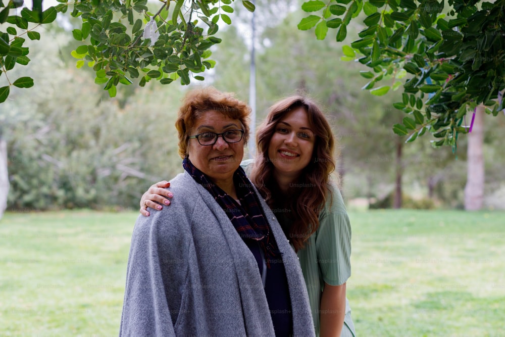 two women standing next to each other under a tree