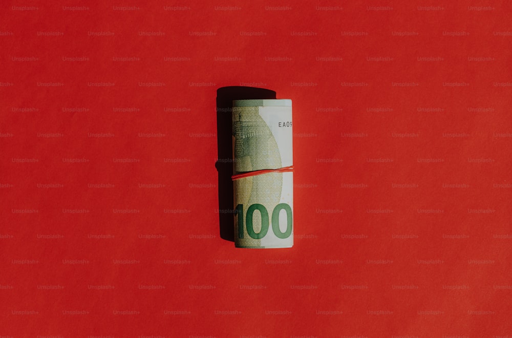 Un rollo de billetes de cien dólares sobre un fondo rojo