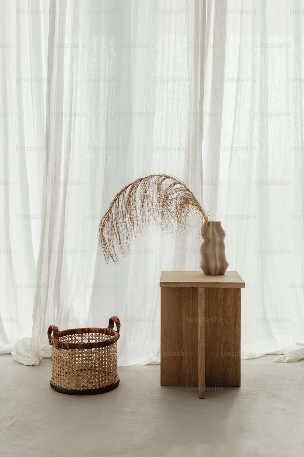 a vase and a basket on a table in front of a curtain