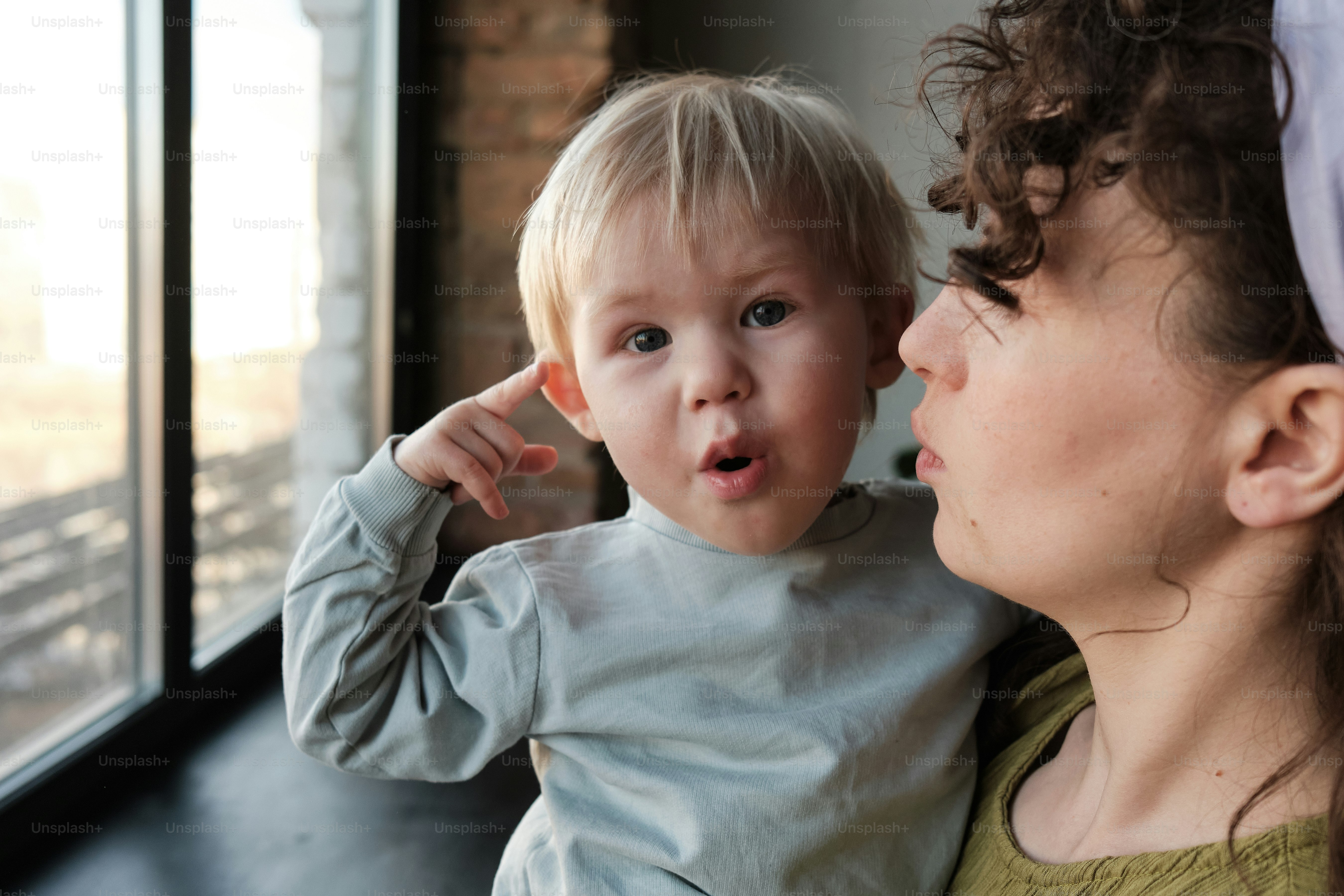 A woman holding a small child near a window photo – Family Image on ...