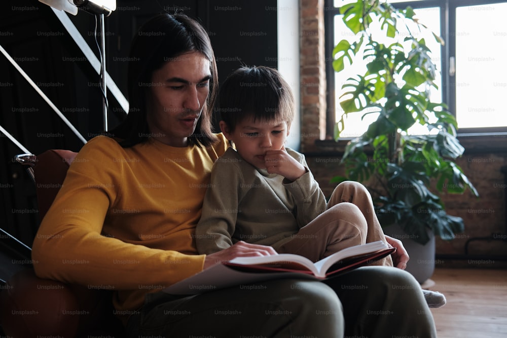 a man and a child sitting on a couch reading a book