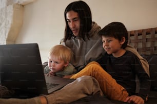 um homem e dois meninos sentados em um sofá olhando para um laptop