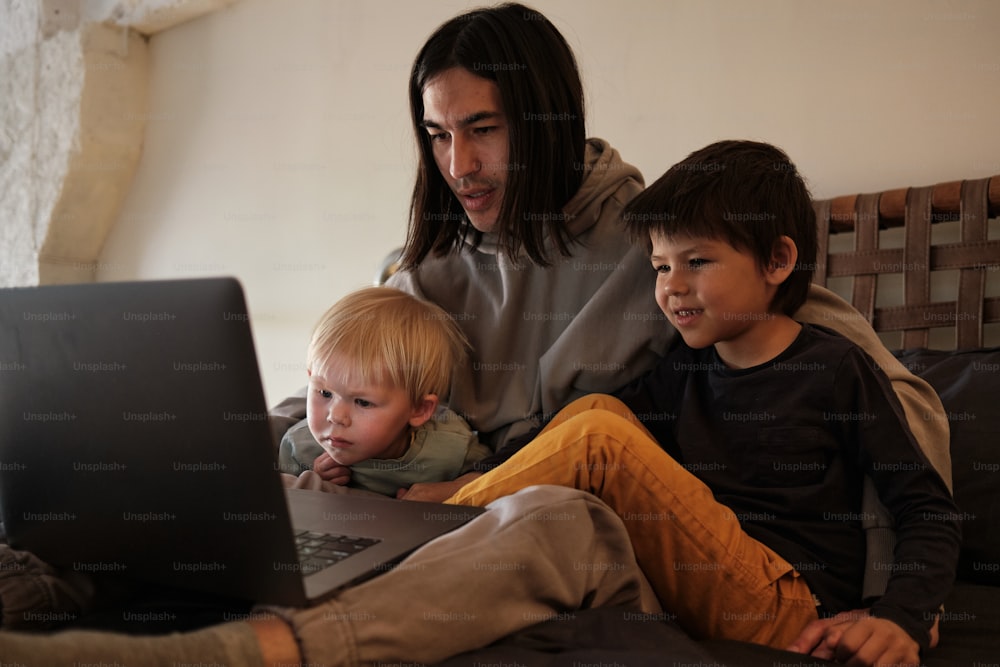 a man and two boys sitting on a couch looking at a laptop