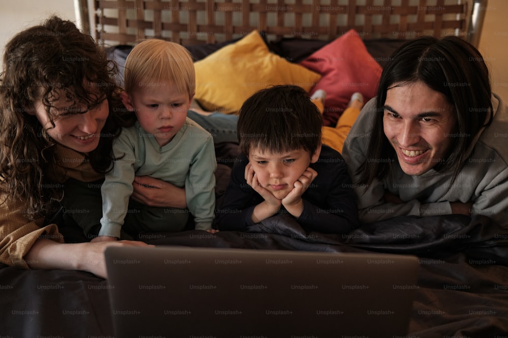 Una familia acostada en la cama mirando una computadora portátil