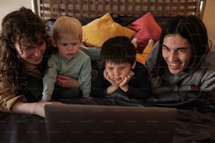 a family laying in bed looking at a laptop