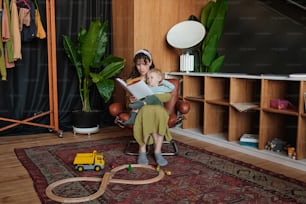 a woman sitting in a chair reading a book to a child