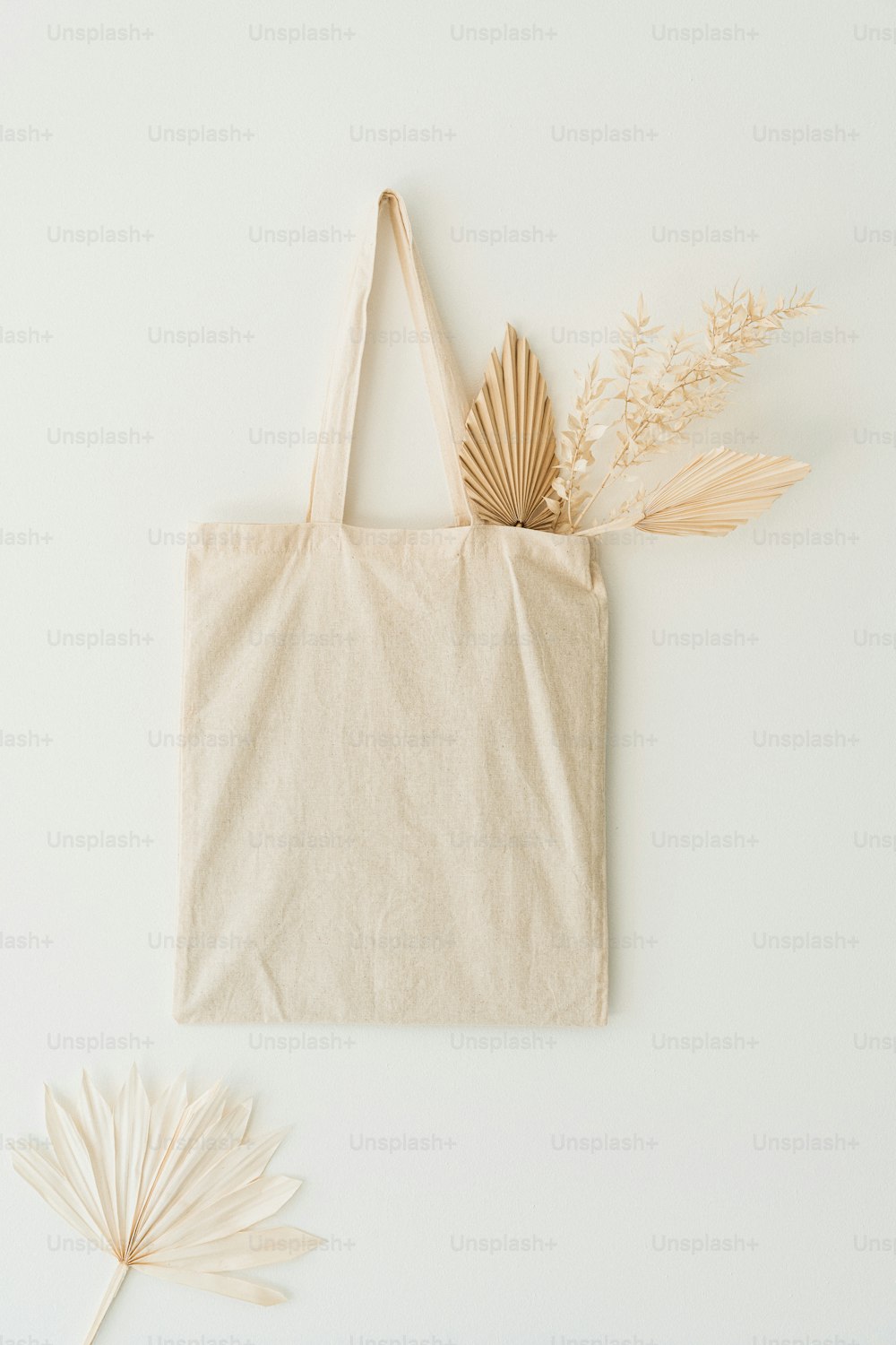 una borsa tote e una foglia di palma su sfondo bianco