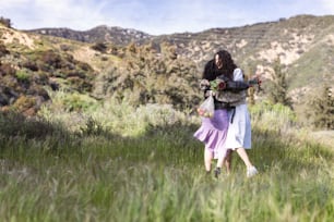 two people walking through a field with mountains in the background