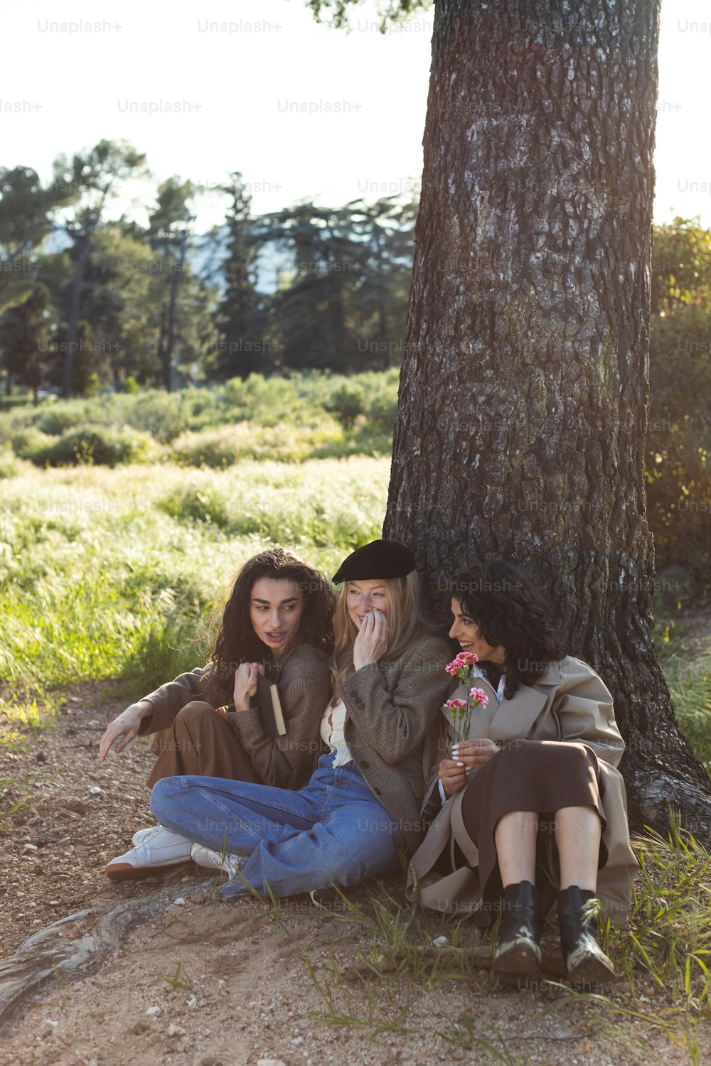 three women sitting under a tree talking on their cell phones