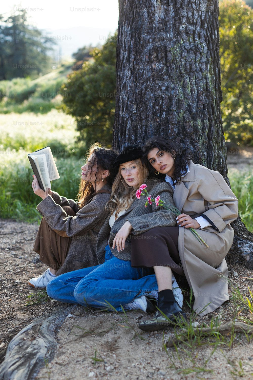 two women sitting under a tree reading a book