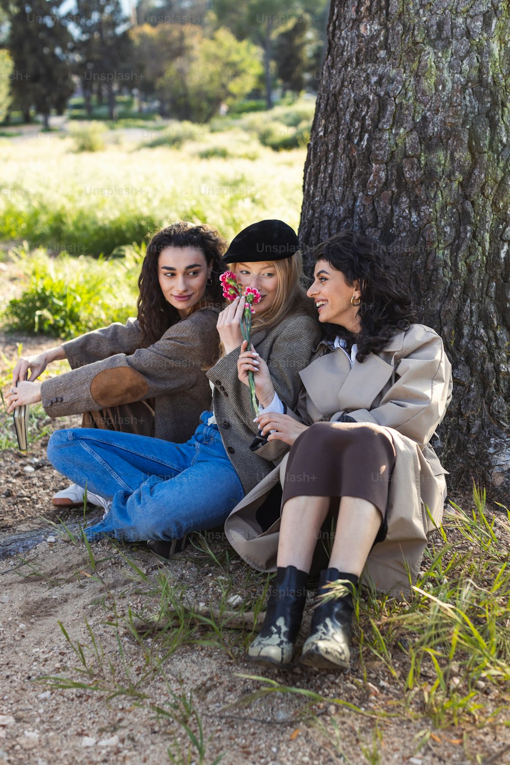 three women sitting on the ground next to a tree