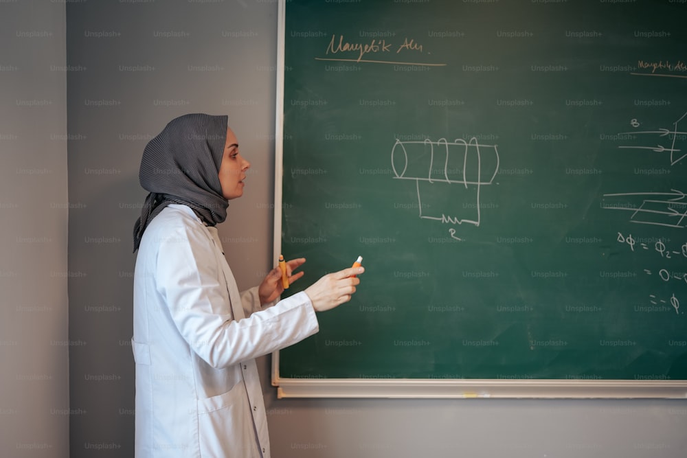 a woman in a hijab writing on a blackboard