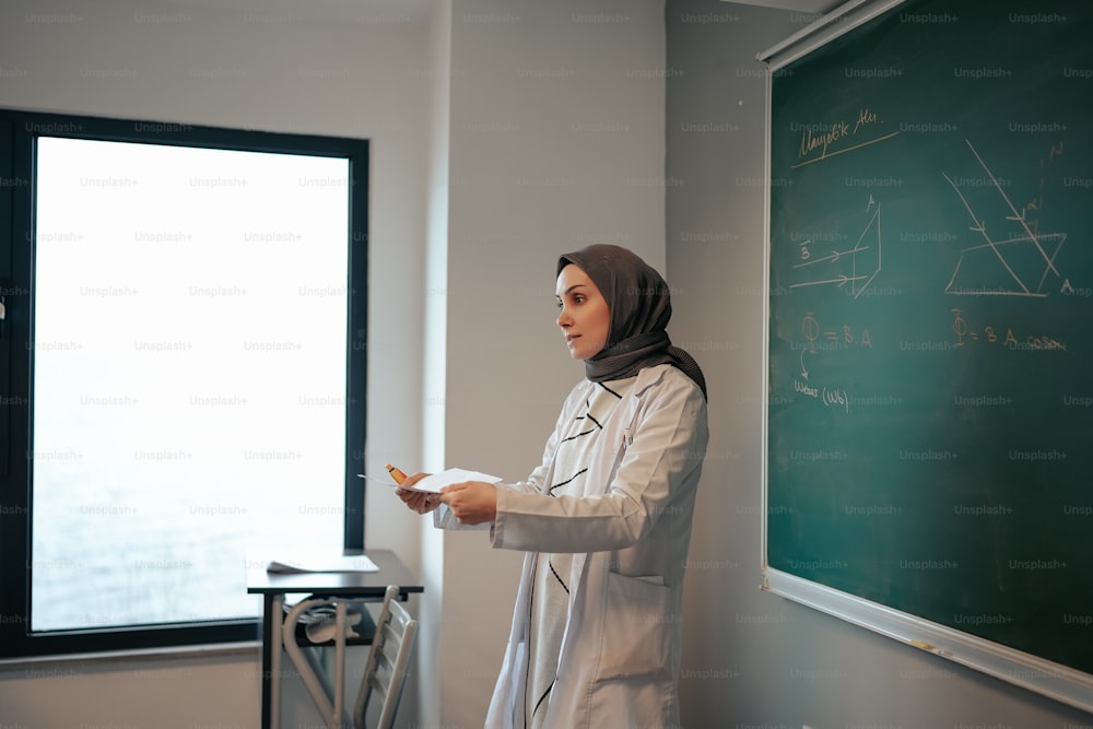 a woman standing in front of a blackboard holding a piece of paper