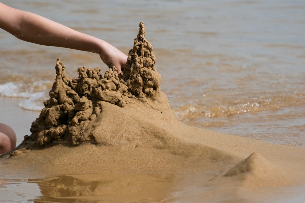 um castelo de areia em uma praia com uma pessoa alcançando-o