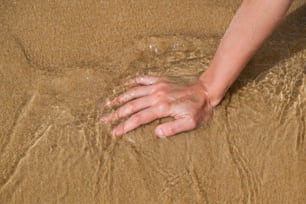 La mano di una persona sulla sabbia di una spiaggia