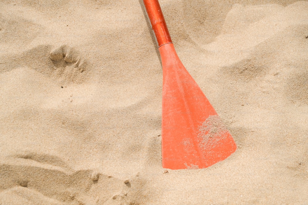 une pagaie rouge posée sur une plage de sable