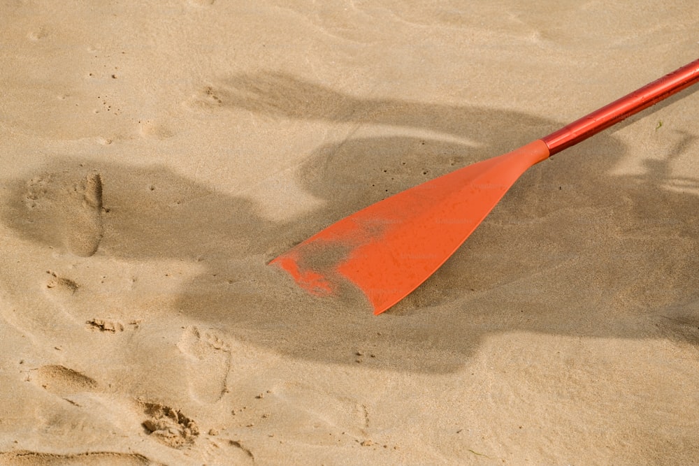 a red paddle sitting on top of a sandy beach