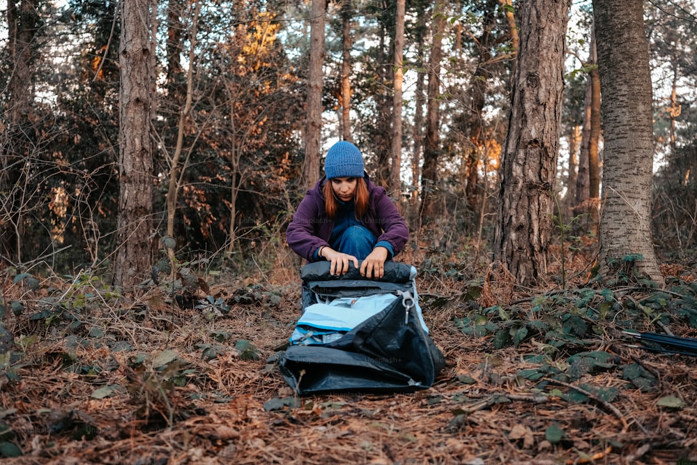 a woman sitting on top of a bag in the woods