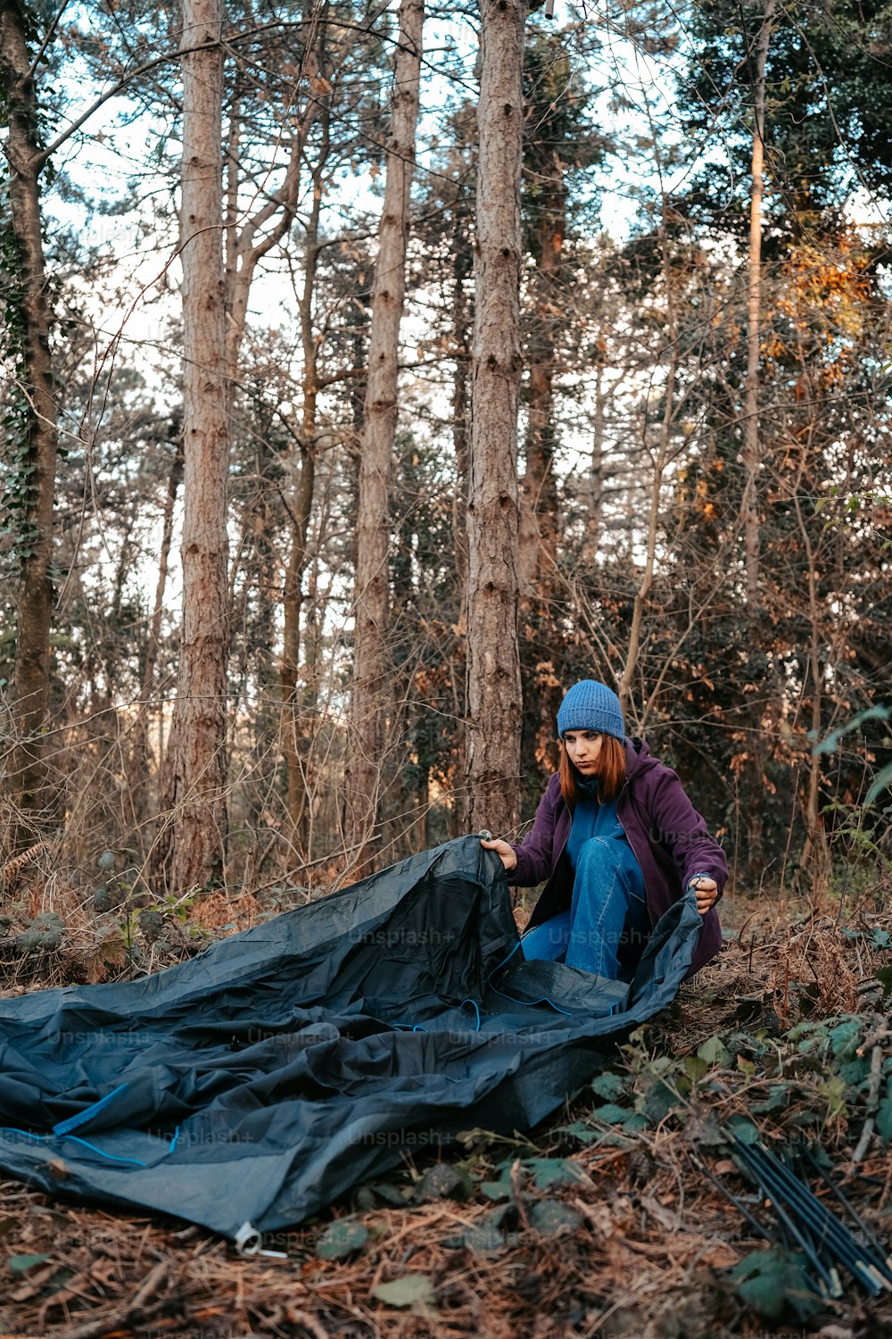 a woman sitting on the ground next to a tarp in the woods