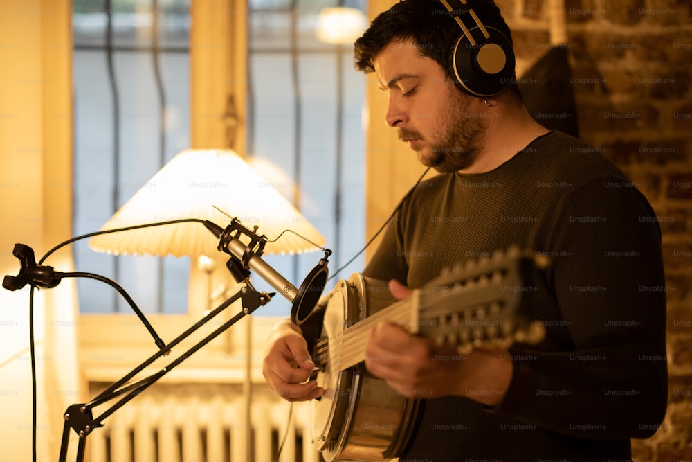 Un hombre con auriculares tocando una guitarra frente a un micrófono