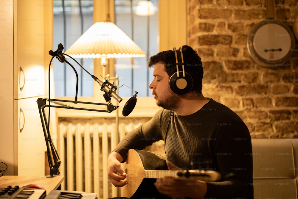 a man sitting in front of a microphone playing a guitar