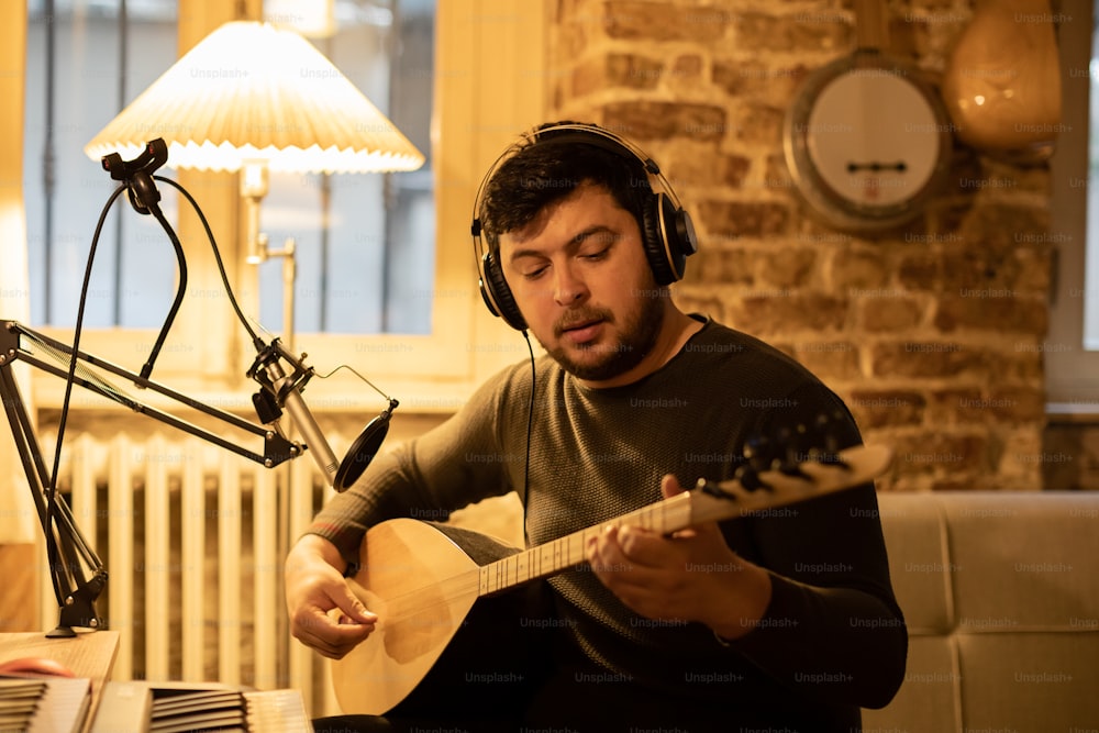 a man sitting in front of a microphone playing a guitar