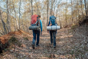 um casal de pessoas com mochilas andando por uma trilha