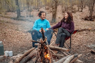 a man and a woman sitting next to a campfire