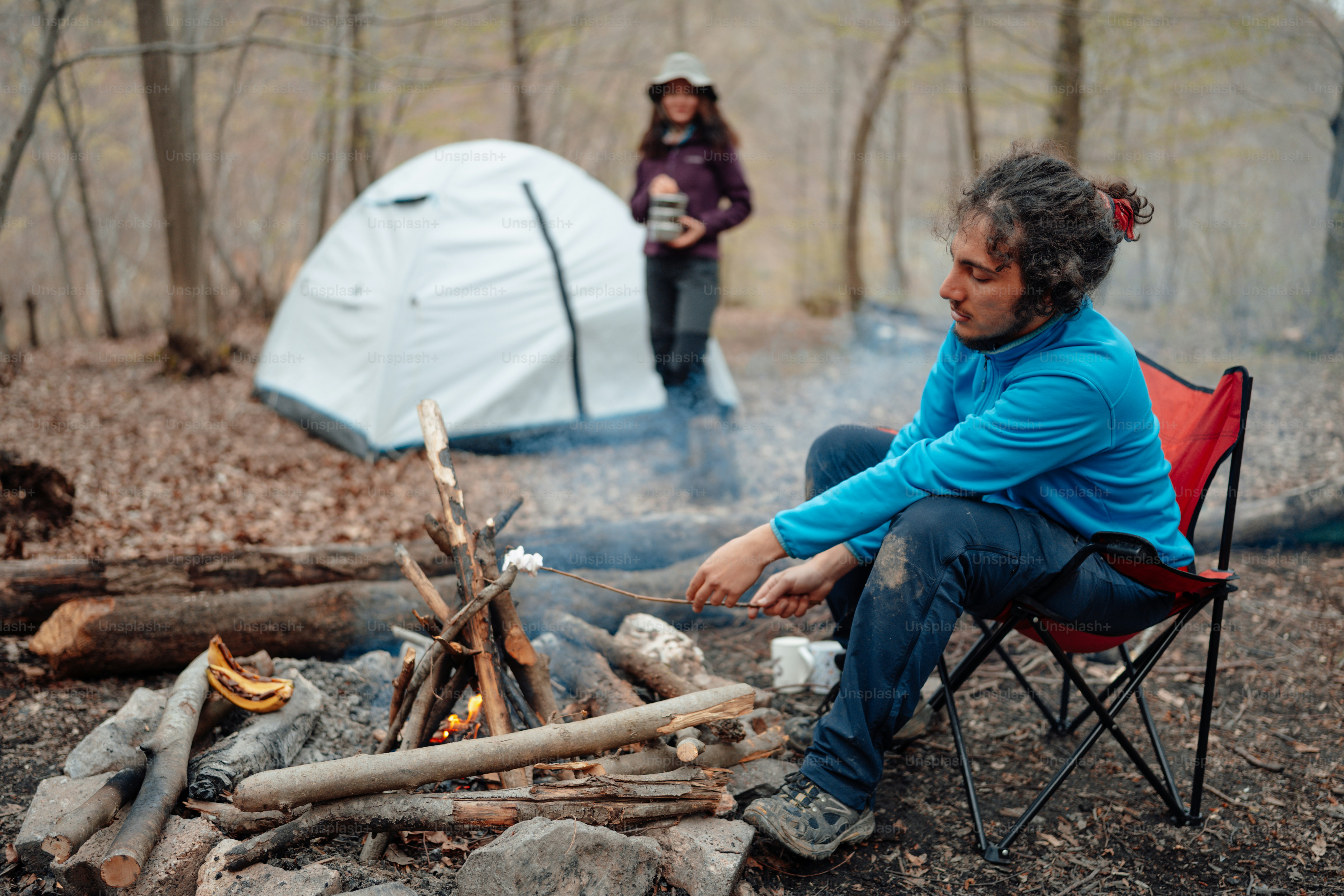 A man sitting in a chair next to a campfire photo – Forest Image on ...