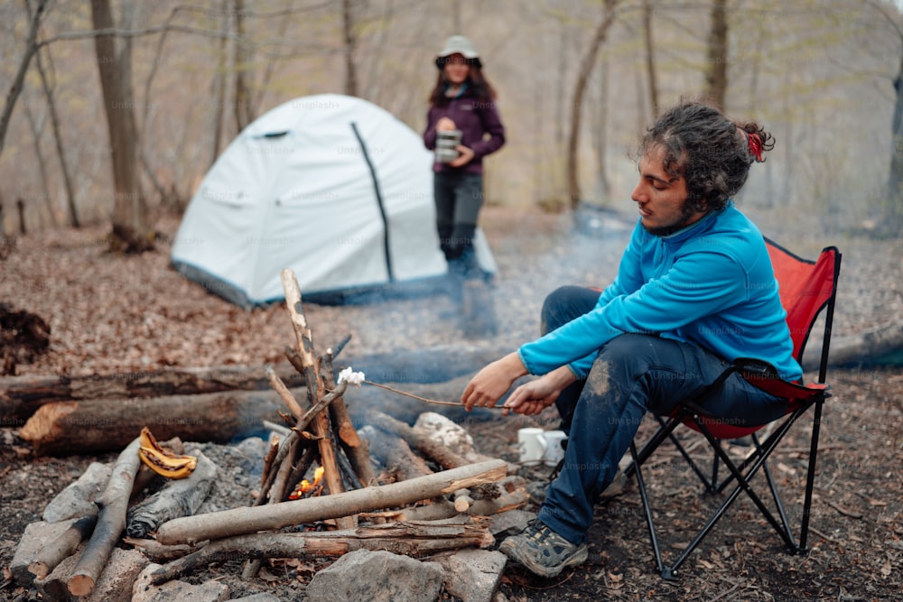 a man sitting in a chair next to a campfire