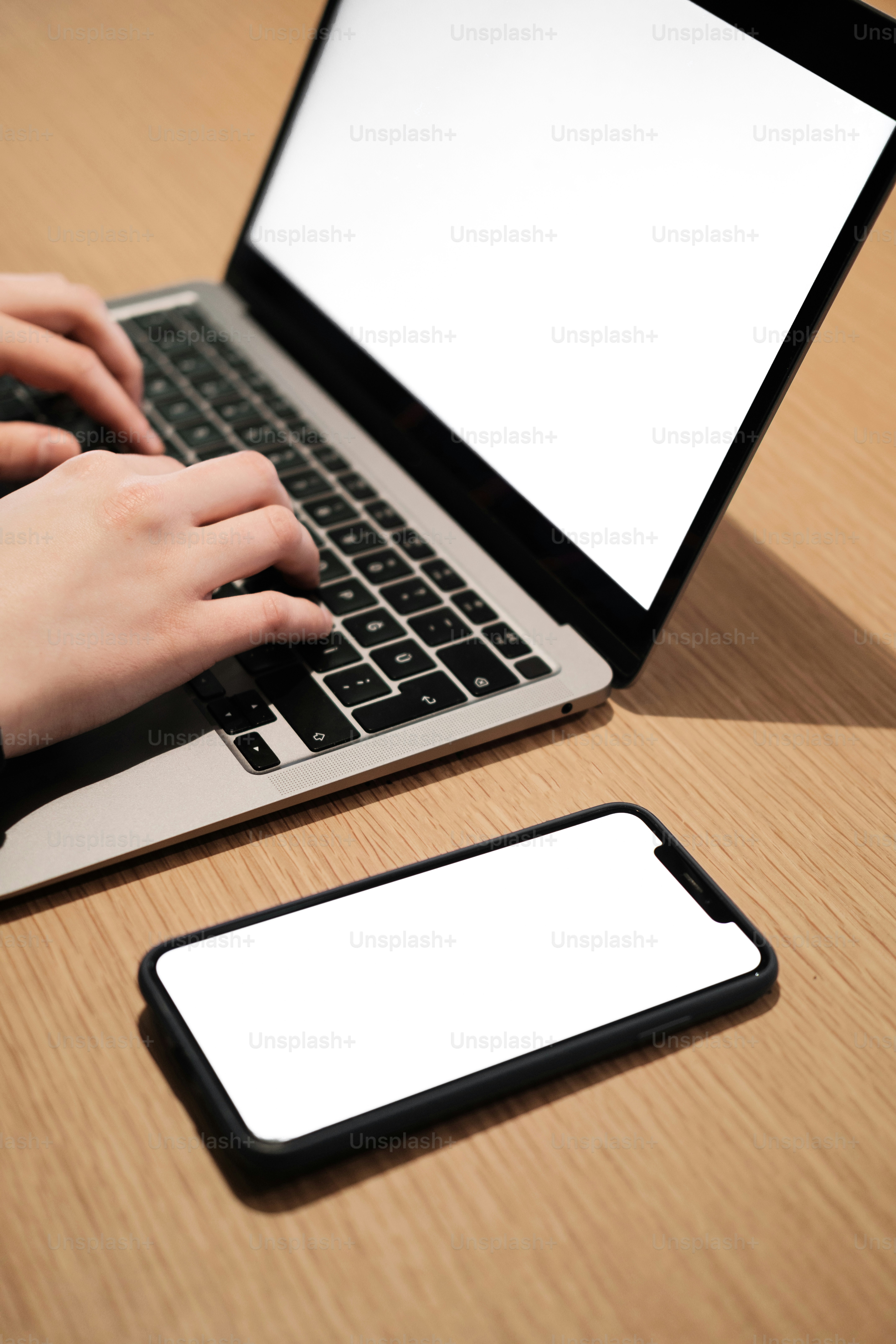 seseorang yang mengetik di laptop dengan ponsel di sebelahnya