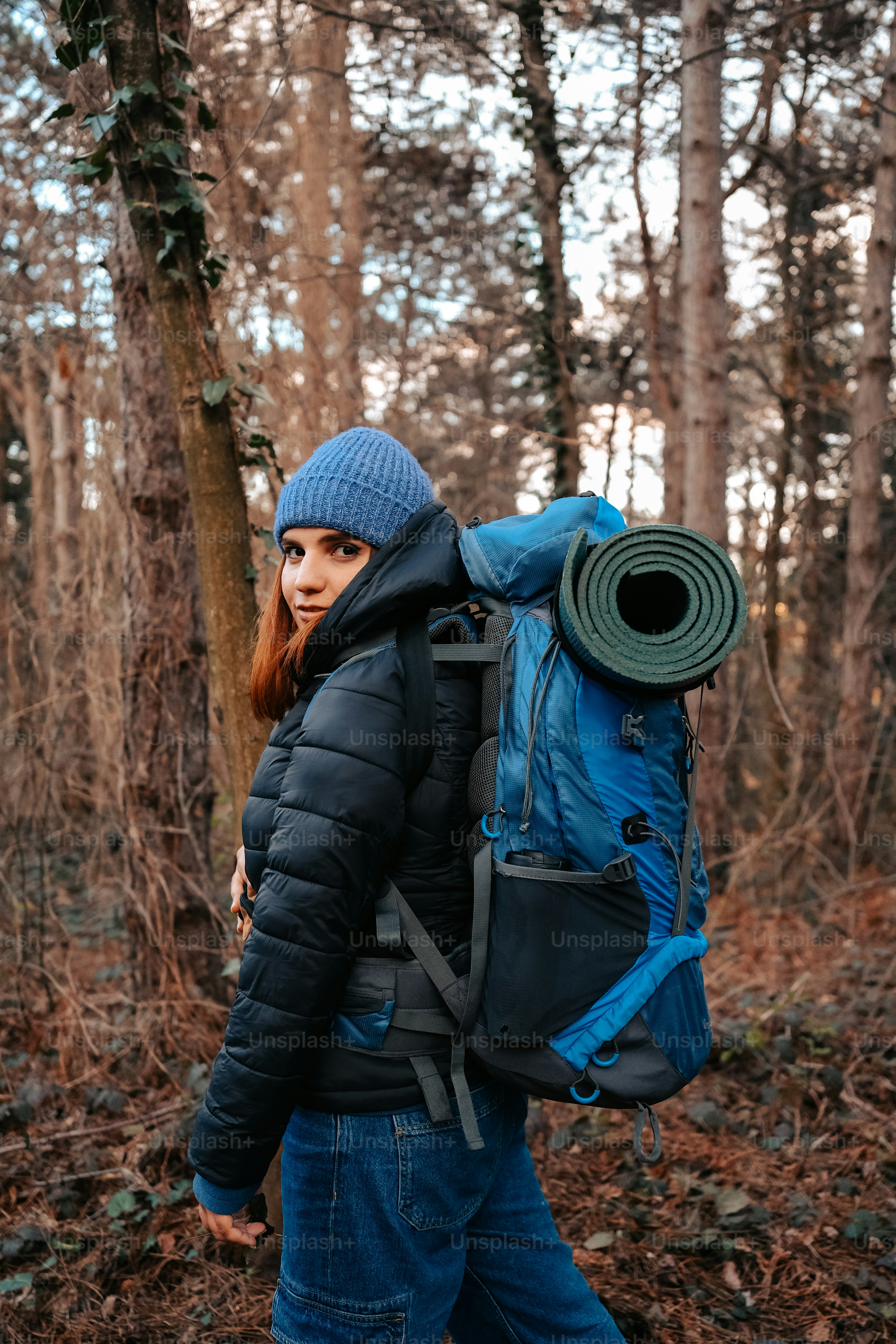 a woman walking through a forest carrying a blue backpack