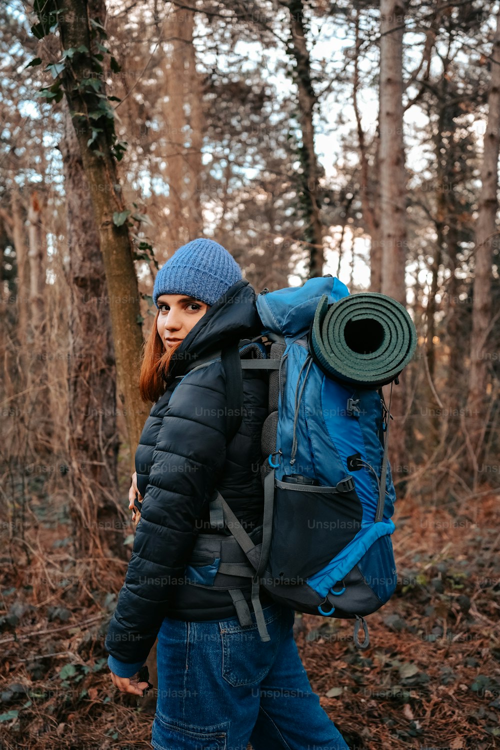 a woman walking through a forest carrying a blue backpack