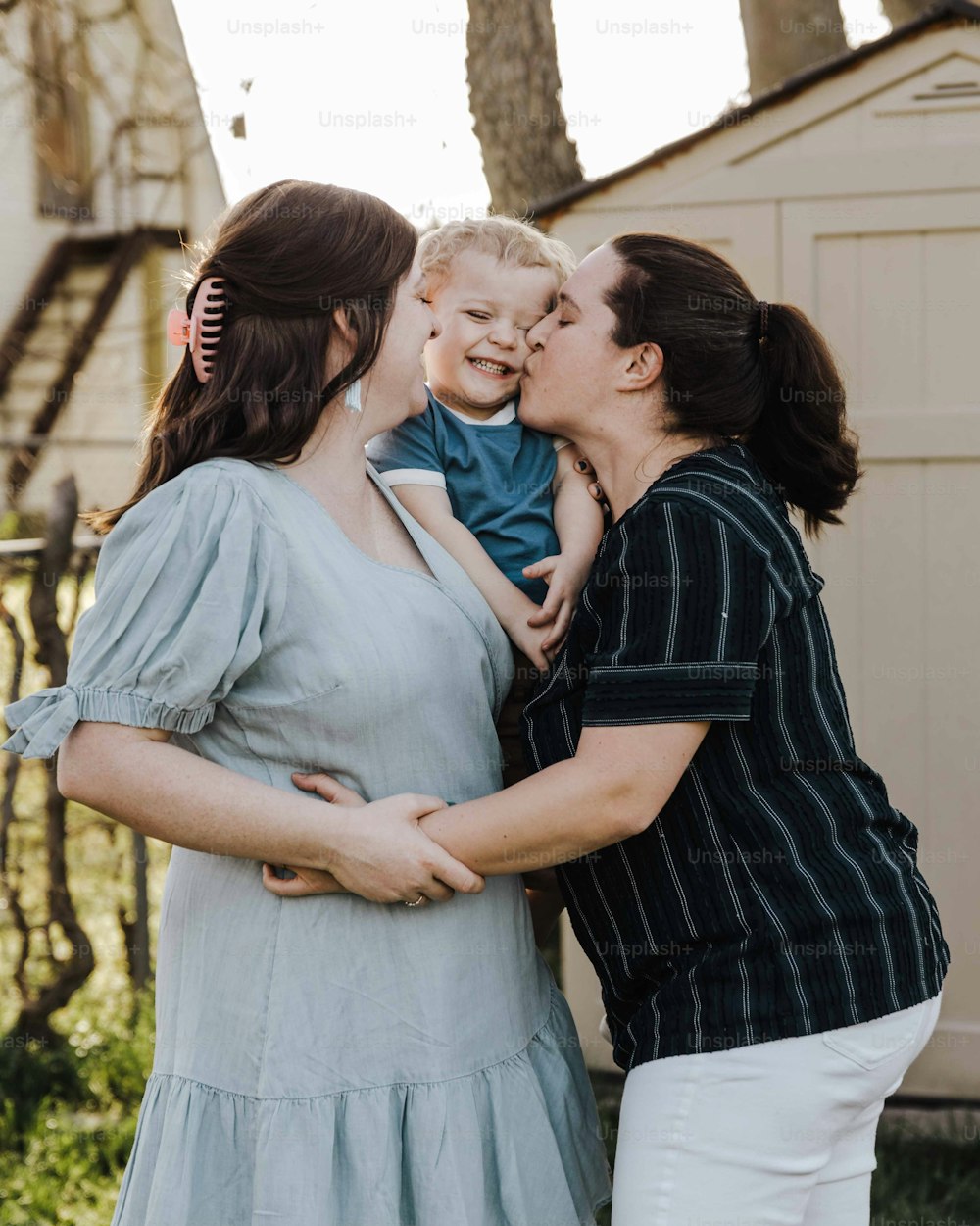 uma mulher segurando um bebê e beijando outra mulher