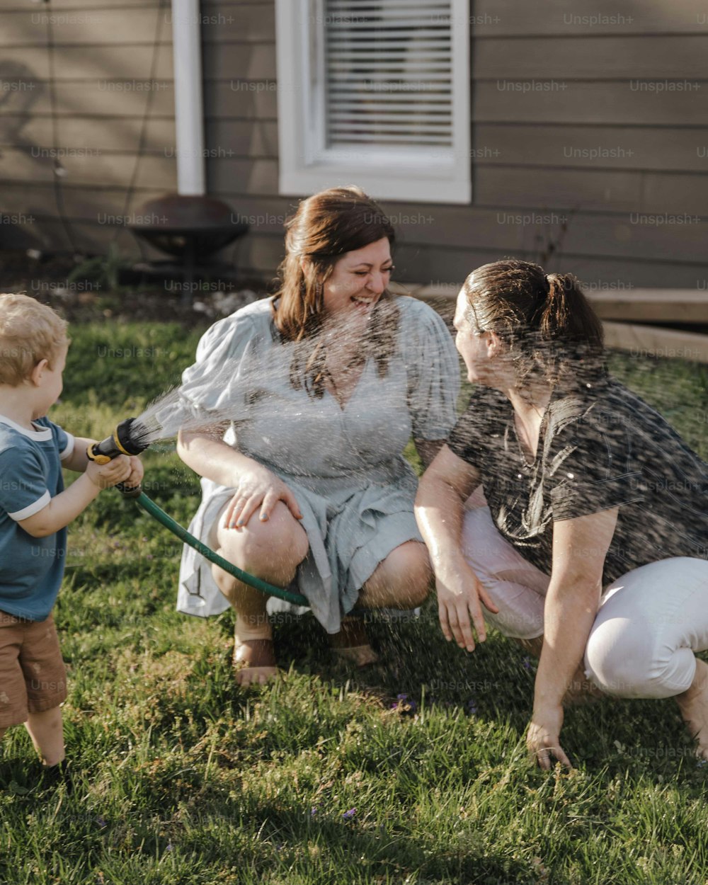 a woman and two children playing with a hose