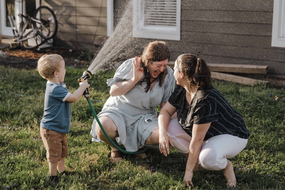 Una mujer y dos niños juegan con una manguera