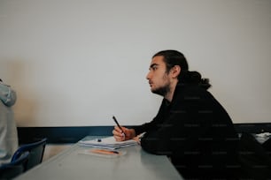 Ein Mann sitzt mit einem Stift in der Hand an einem Tisch