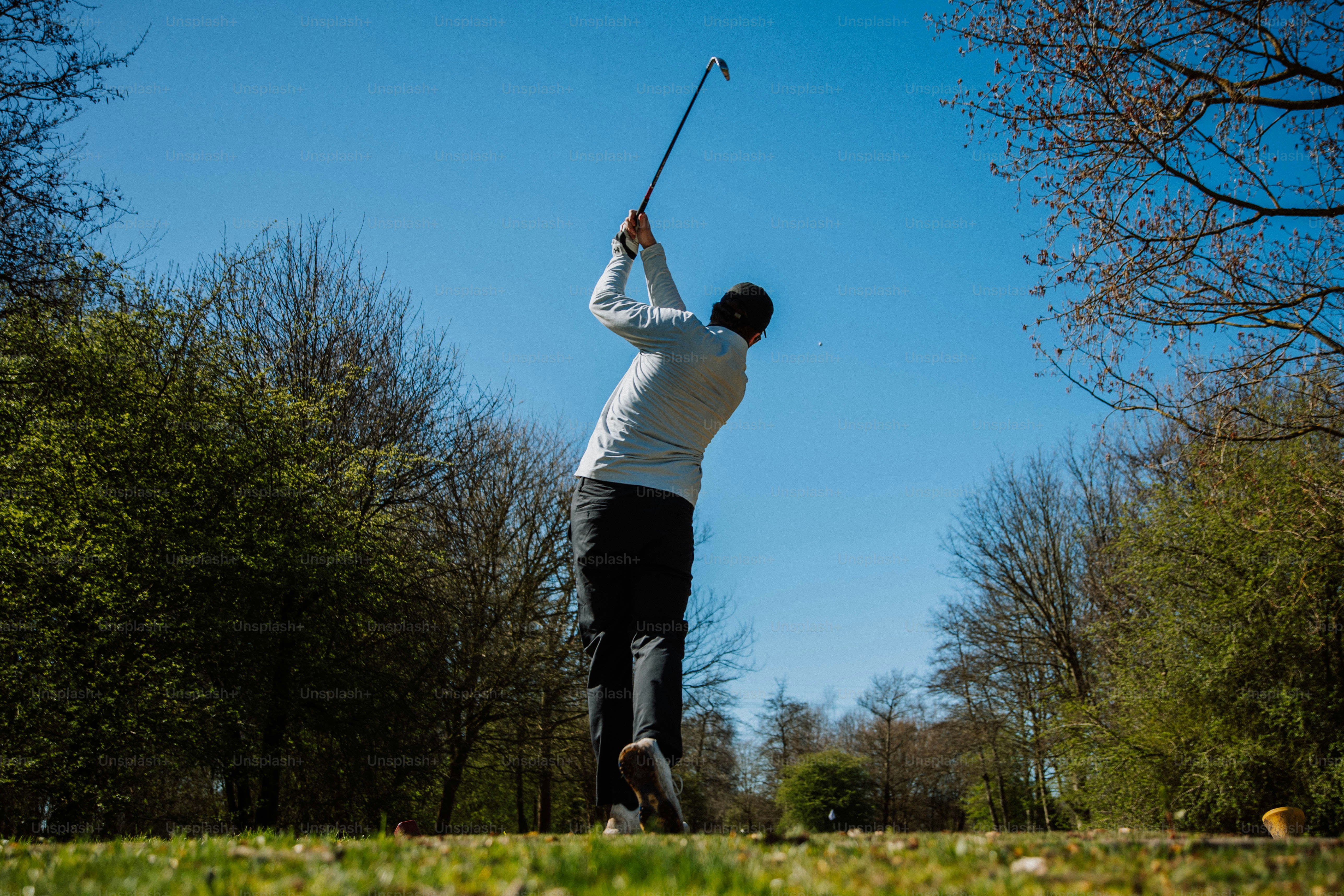 Seorang pria mengayunkan tongkat golf di hari yang cerah