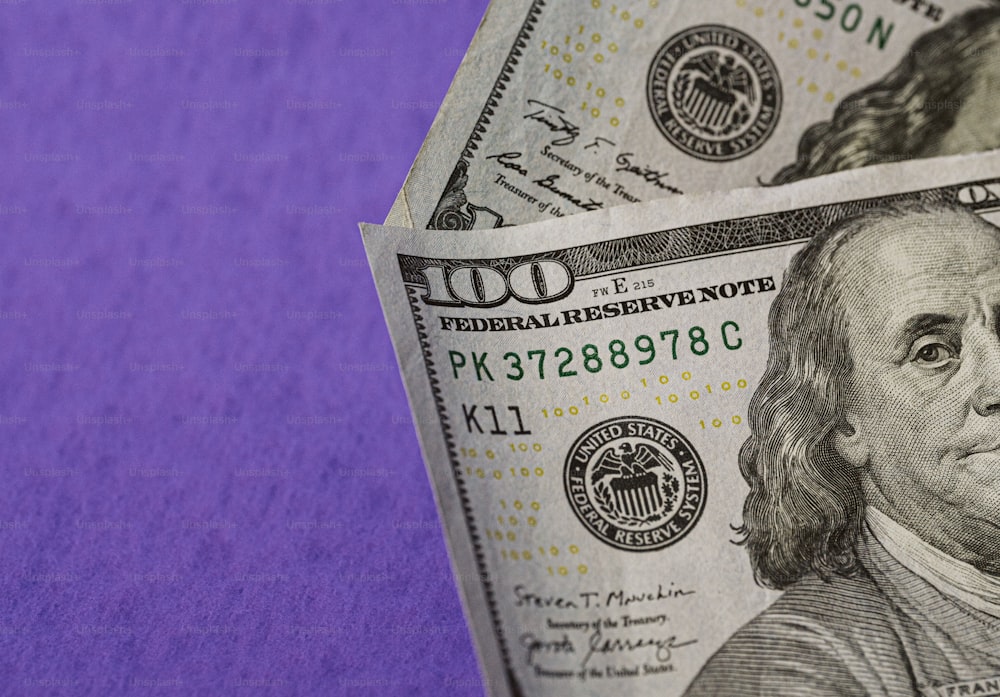 a stack of one hundred dollar bills on a purple background