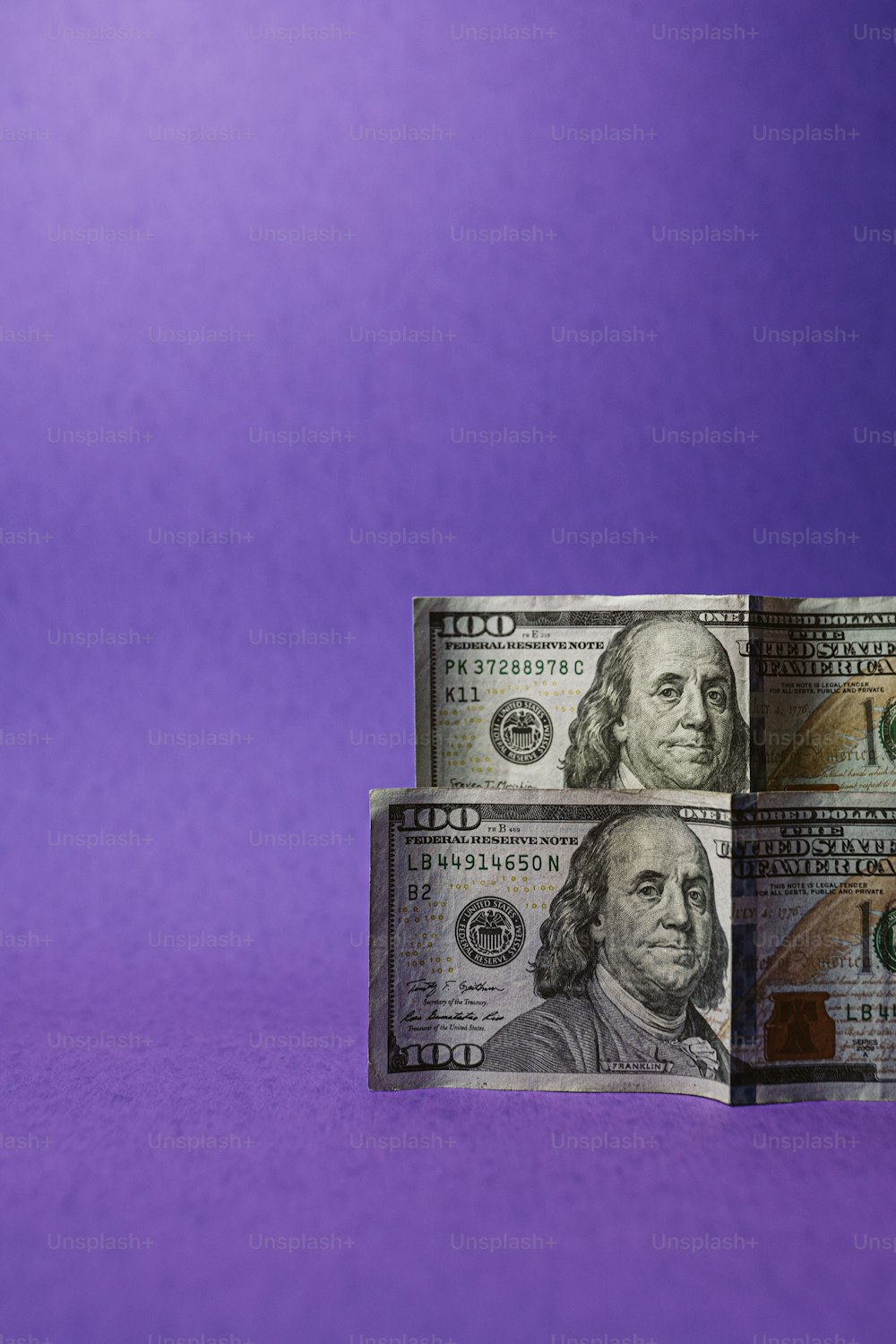 three stacks of one hundred dollar bills on a purple background