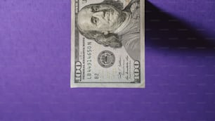uma nota de cem dólares deitada em uma superfície roxa